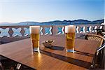 Two cold beer glasses and a plate of olives in a table of a terrace next to the sea in Spain.