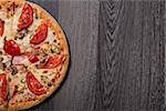 Top view of delicious Italian pizza with ham and tomatoes on gray wooden table