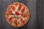 High angle view of delicious Italian pizza with ham and tomatoes on gray wooden table