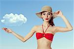 Young girl in swimsuit is holding hat and pointing a cloud by hand . with expresssion on face