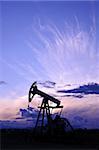 Oil and gas industry. Silhouette oil pump on a purple sunset sky background.