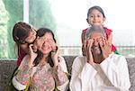 Indian family living lifestyle at home. Cute girls in traditional sari costume covering father and mother eyes. Asian parents and children.