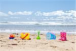 Brightly colored plastic beach toys on the beach with the ocean and clouds in background