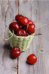 Red Sweet Cherries in Green Wicker Basket isolated on Rustic Wooden background