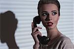 vintage woman with elegant hair-style and worried expression talking on the retro phone