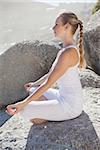 Blonde woman sitting in lotus pose on a rock on a sunny day