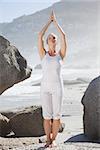 Blonde woman standing in tree pose on a rock on a sunny day