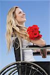 Wheelchair bound blonde smiling on the beach holding roses on a sunny day