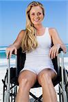 Wheelchair bound blonde sitting on the beach smiling at camera on a sunny day