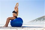 Fit blonde sitting on exercise ball at the beach on a sunny day