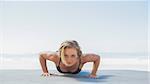 Fit blonde in plank position on the beach on a sunny day