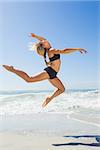 Fit blonde jumping gracefully on the beach on a sunny day