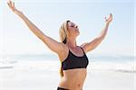 Fit blonde standing on the beach with arms outstretched on a sunny day