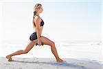 Fit blonde doing weighted lunges on the beach on a sunny day