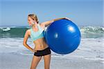 Fit woman standing on the beach holding exercise ball on a sunny day