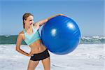 Fit woman standing on the beach holding exercise ball on a sunny day