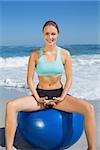 Fit woman sitting on exercise ball at the beach on a sunny day