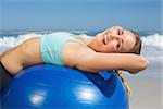 Fit woman lying on exercise ball at the beach stretching on a sunny day