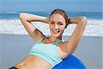 Fit woman lying on exercise ball at the beach doing sit ups on a sunny day