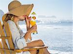 Smiling blonde relaxing in deck chair by the sea sipping cocktail on a sunny day