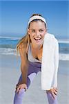 Sporty smiling blonde standing on the beach with towel on a sunny day