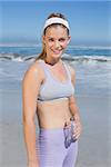 Sporty happy blonde standing on the beach with bottle on a sunny day