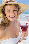 Pretty smiling blonde holding cocktail on the beach on a sunny day