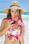 Pretty blonde in floral garland sipping cocktail on the beach on a sunny day