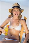 Pretty smiling blonde relaxing in deck chair on the beach with cocktail on a sunny day