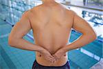 Fit swimmer touching his back by the pool at the leisure center