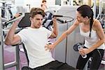 Fit man using weights machine for arms with his trainer at the gym