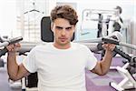 Fit man using weights machine for arms looking at camera at the gym
