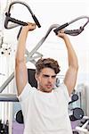 Fit focused man using weights machine for arms at the gym