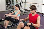 Man and woman working out on the rowing machine at the gym