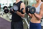 Fit couple lifting dumbbells together at the gym