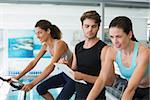 Fit women in a spin class with trainer taking notes at the gym