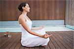 Peaceful brunette in white sitting in lotus pose in health spa