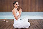 Content brunette in white sitting in lotus pose smiling at camera in health spa
