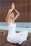 Content brunette in white sitting in lotus pose with hands together in health spa