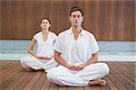 Peaceful couple in white sitting in lotus pose together in health spa