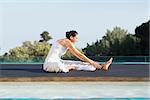 Peaceful brunette in janu sirsasana yoga pose poolside on a sunny day at the spa