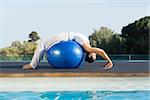 Peaceful brunette in cobra pose over exercise ball poolside on a sunny day at the spa