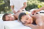 Attractive couple enjoying hot stone massage poolside outside at the spa