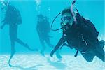 Friends on scuba training submerged in swimming pool one looking to camera on their holidays