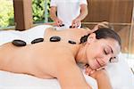 Happy friends lying on massage tables with hot stones on their backs in the health spa