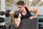 Focused bodybuilder lifting heavy black dumbbell at the gym