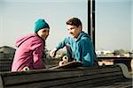 Teenage boy and girl sitting on bench outdoors with skateboard, industrial area, Mannheim, Germany