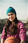 Close-up portrait of teenage girl outdoors, holding basketball and wearing toque, smiling and looking at camera, Germany