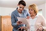 Teenage boy helping Grandmother sitting in walker at home, filling out paperwork, Germany