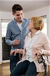 Teenage boy helping Grandmother sitting in walker at home, getting glass of water, Germany